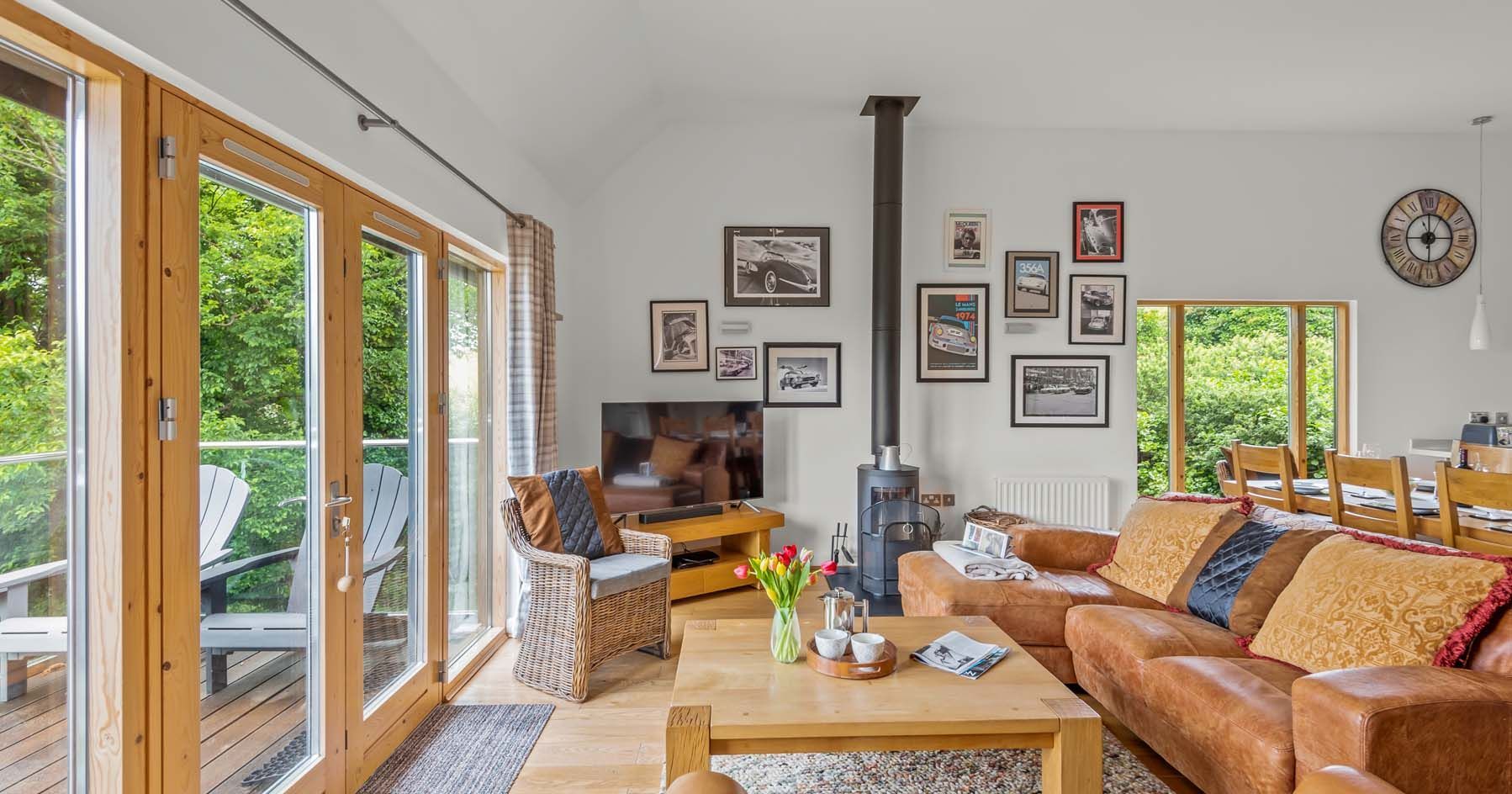 Cozy living room with large windows, brown leather sofas, wood stove, and wall art