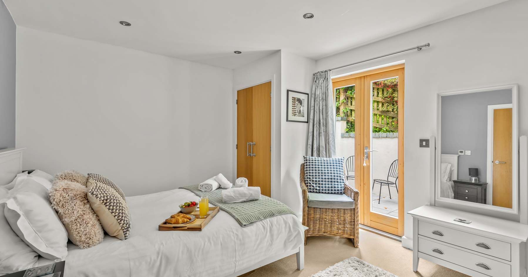 Bright modern bedroom with double bed, vanity, chair, and doors to patio