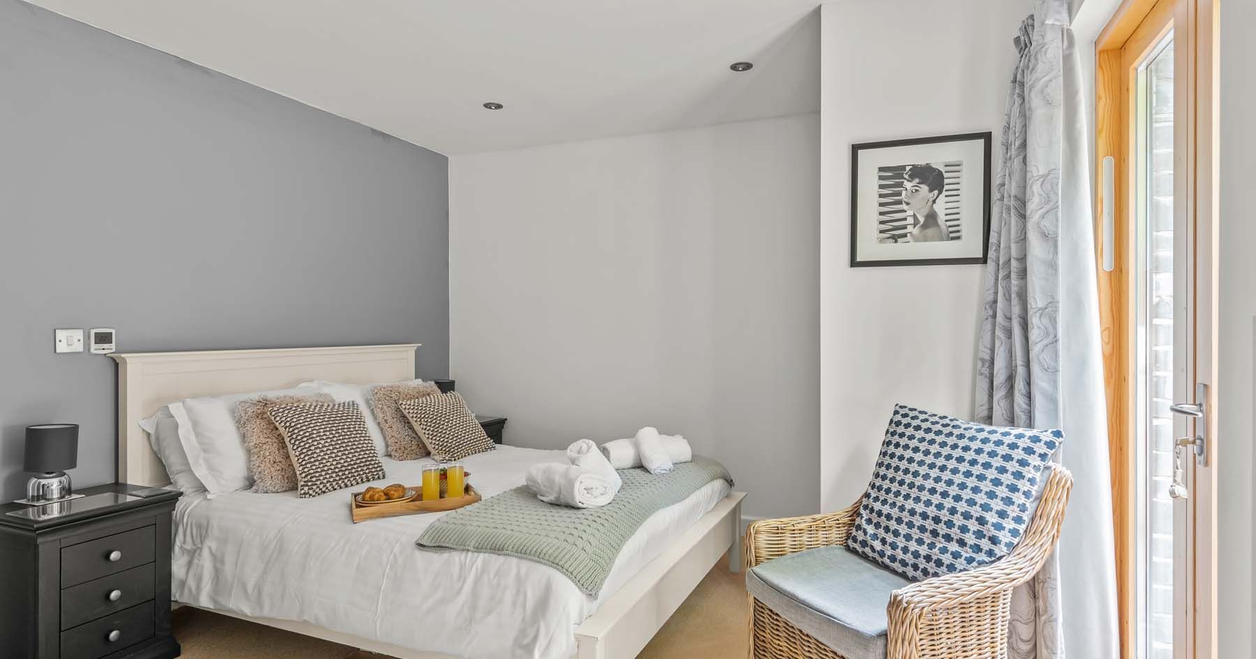 Cozy contemporary bedroom with a neatly made bed, side table, wicker chair and framed art on the wall.
