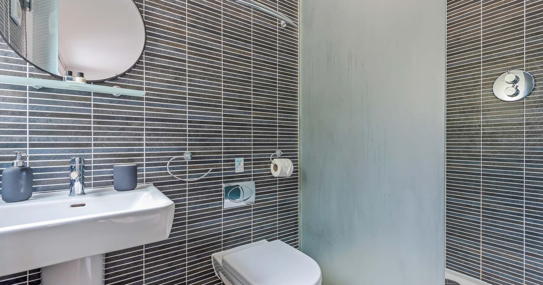 Modern bathroom with dark striped tiles, white sink, toilet, and glass shower panel