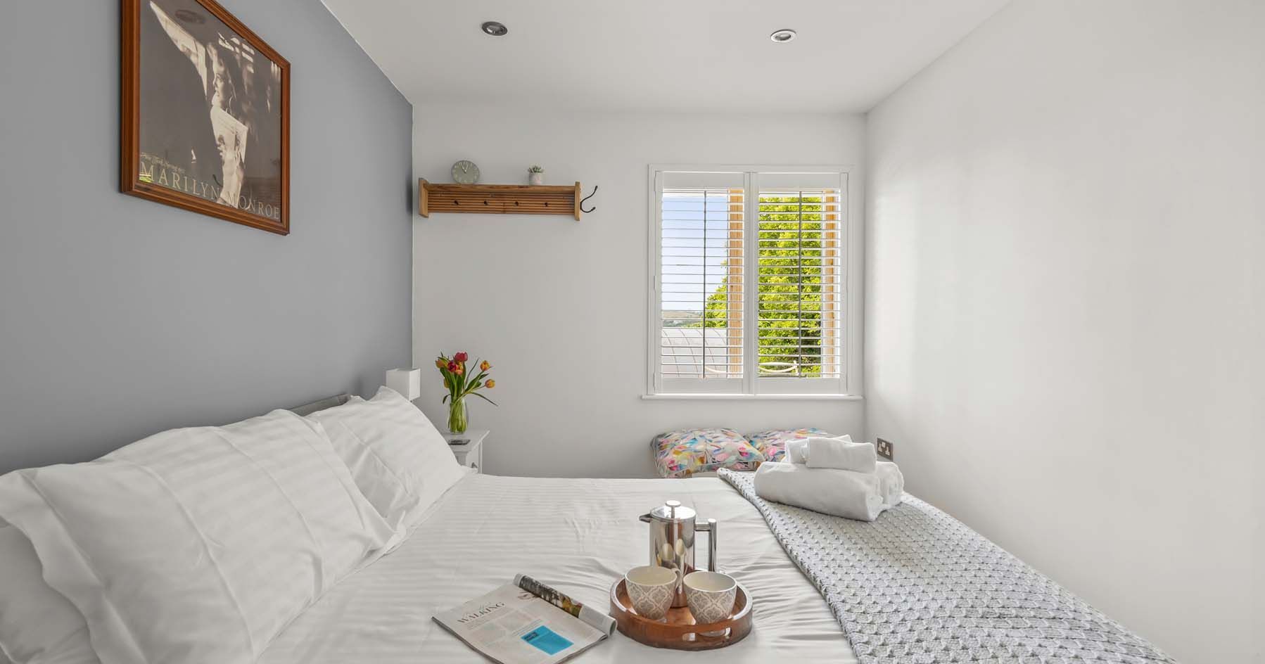 Bright bedroom with white bedding, a tray with cups, and large window.