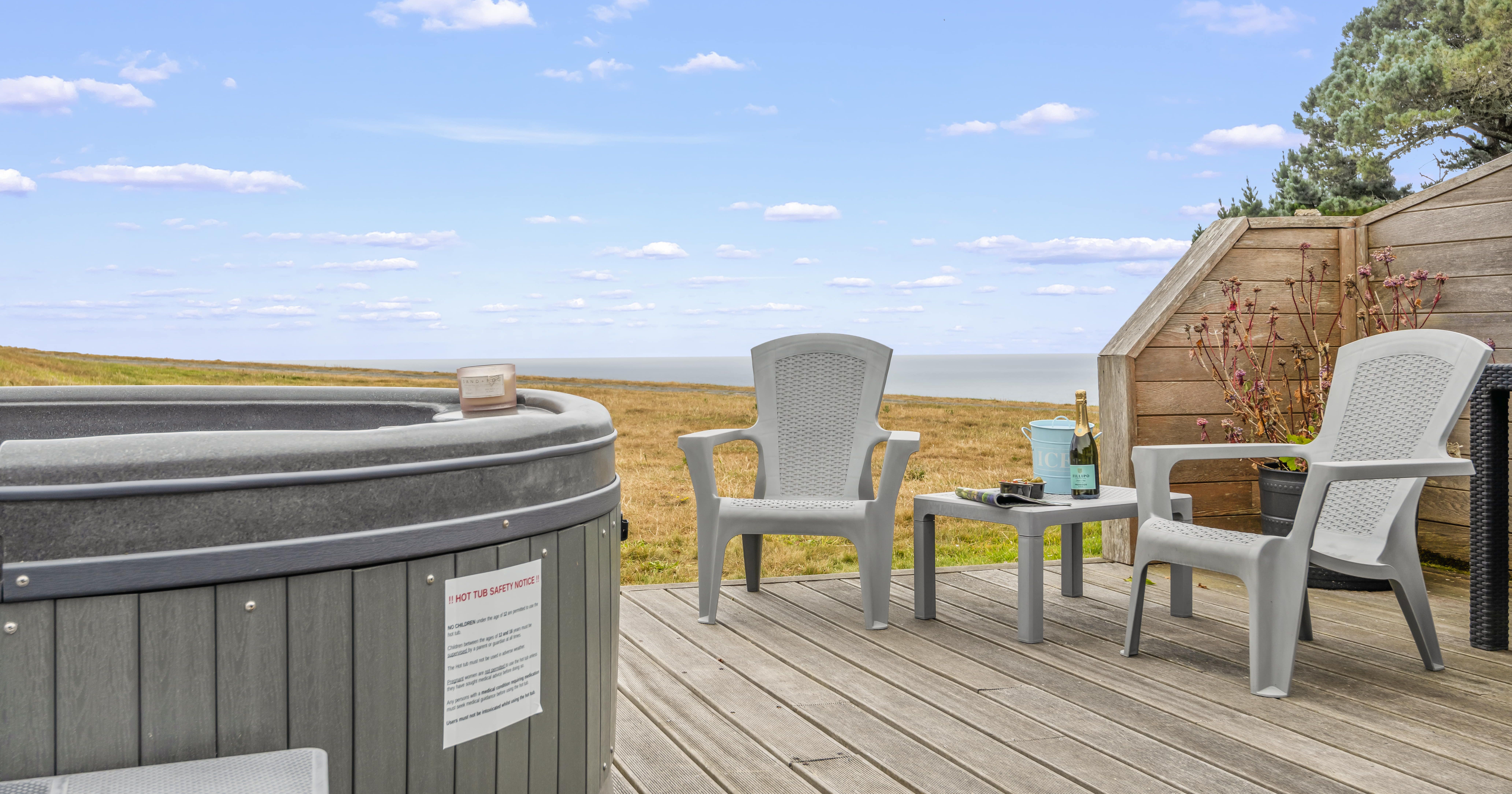 Outdoor deck with hot tub, patio chairs, and a view of fields leading to the sea