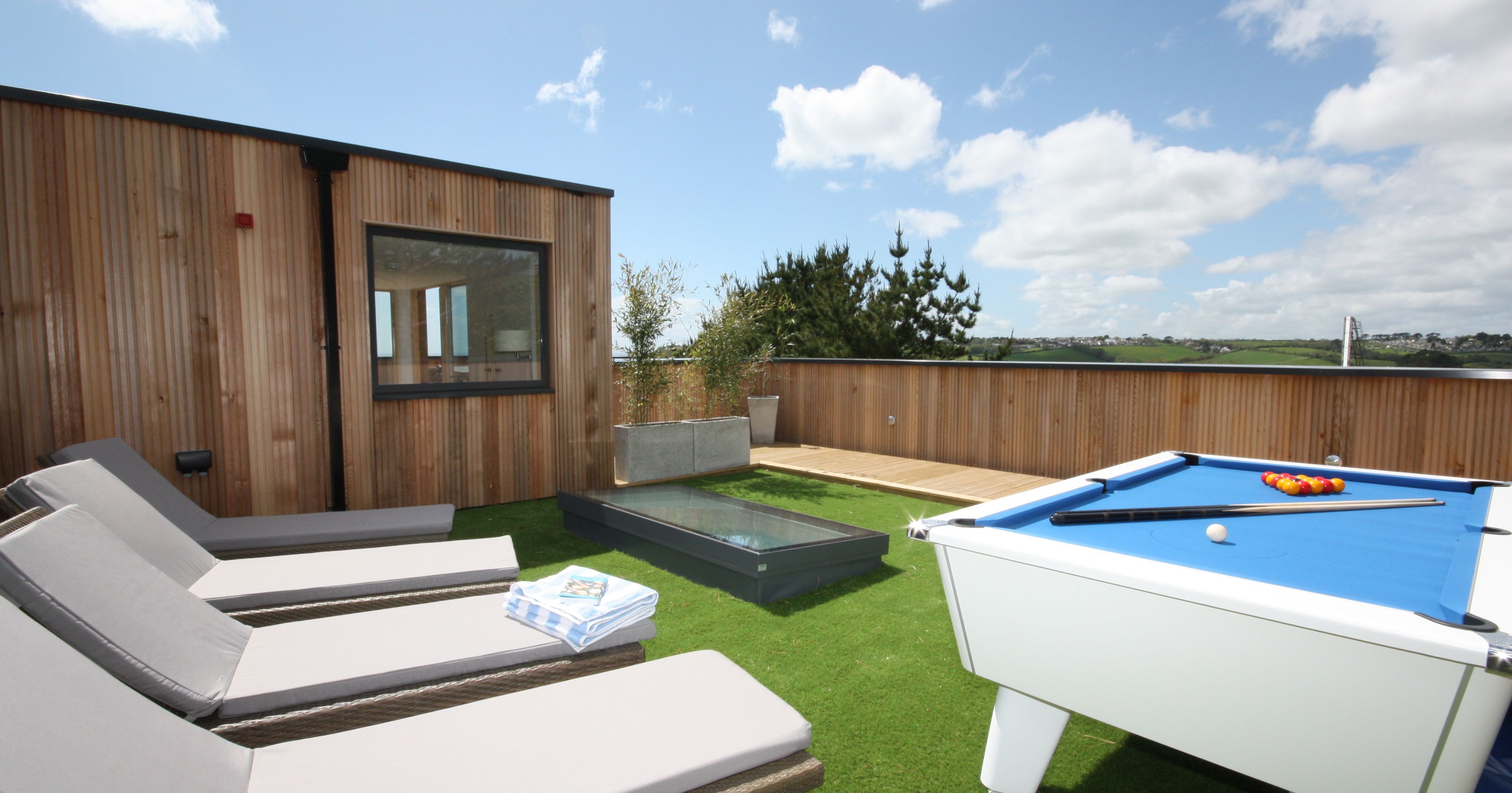 Modern outdoor patio with sun loungers and a pool table on artificial grass