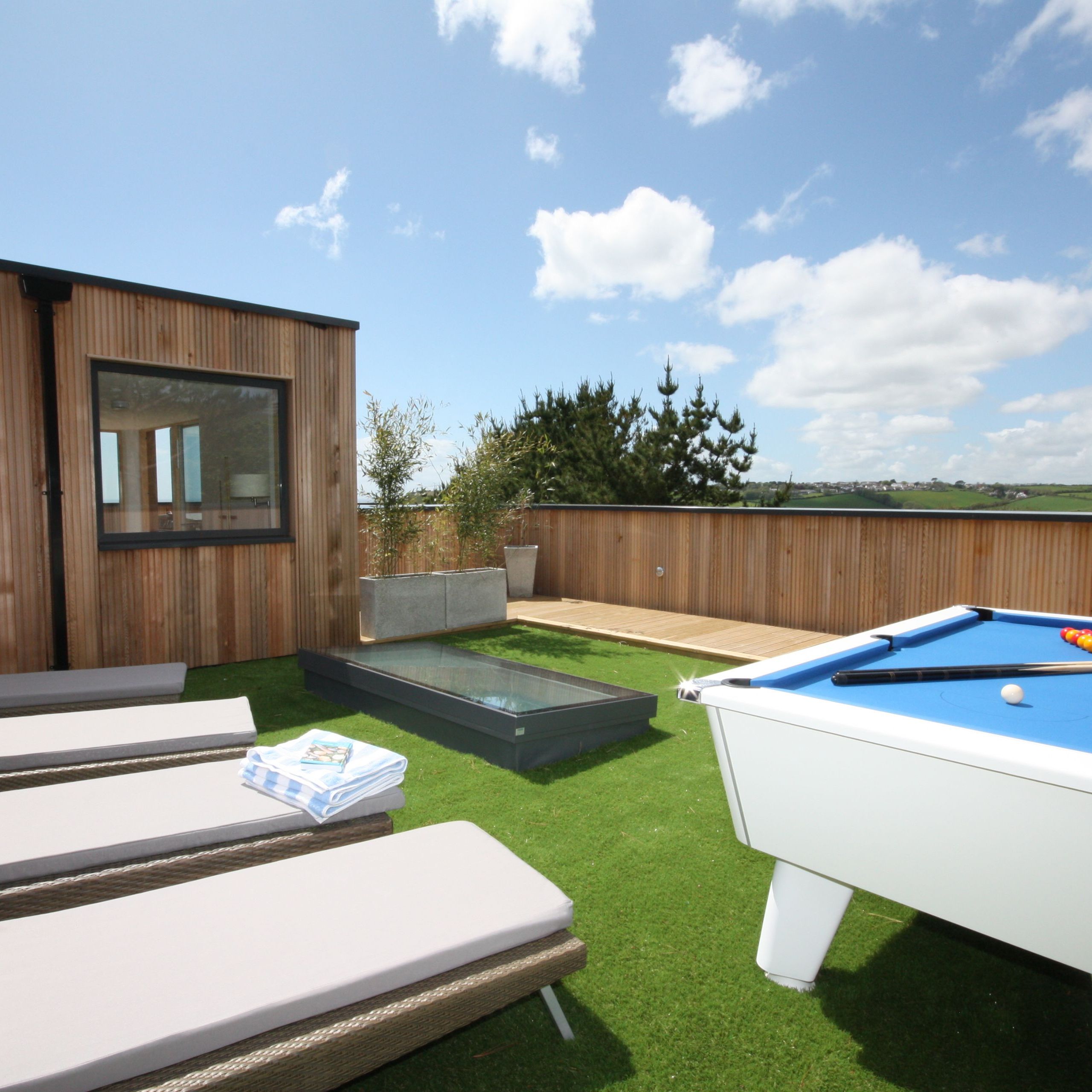 Modern outdoor patio with sun loungers and a pool table on artificial grass