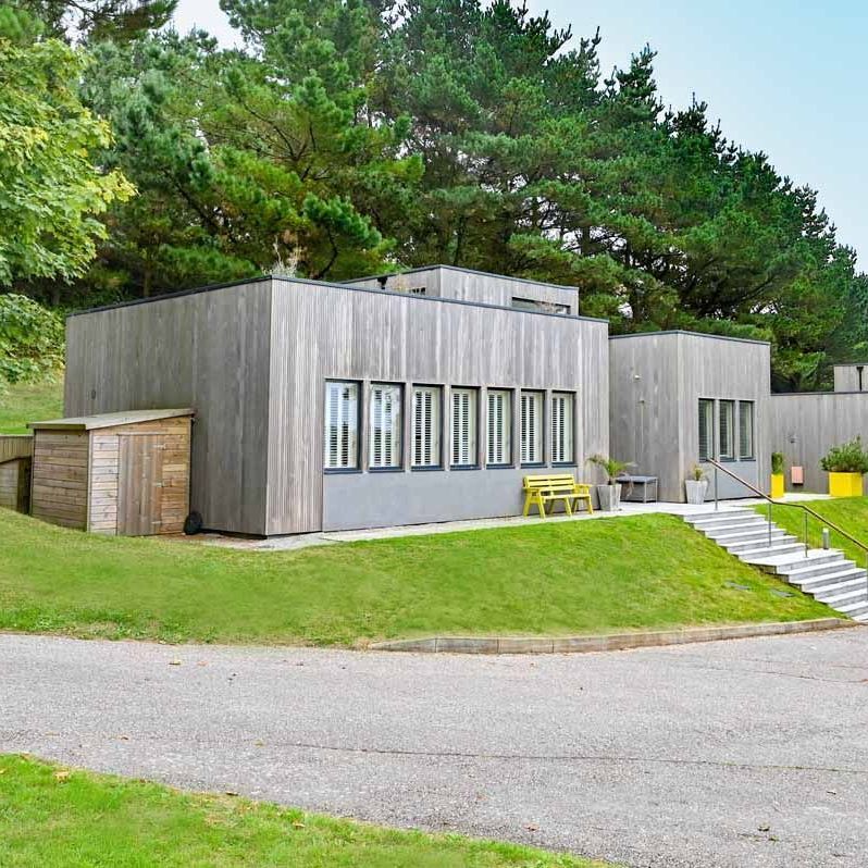 Modern wood-paneled building with flat roofs surrounded by trees and greenery.