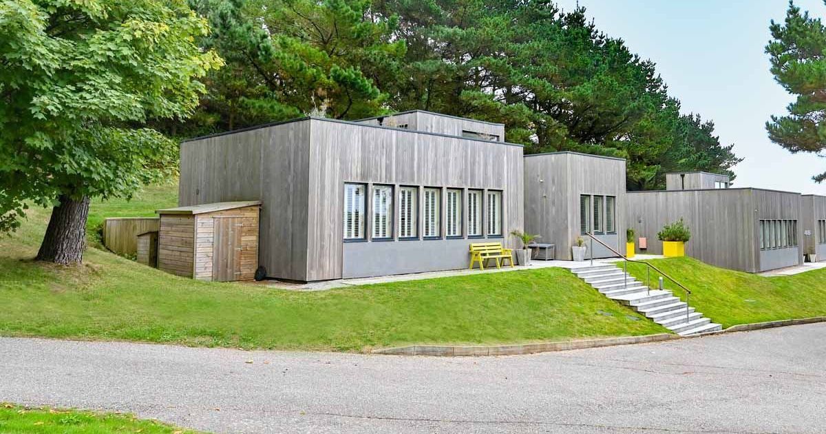 Modern wood-paneled building with flat roofs surrounded by trees and greenery.