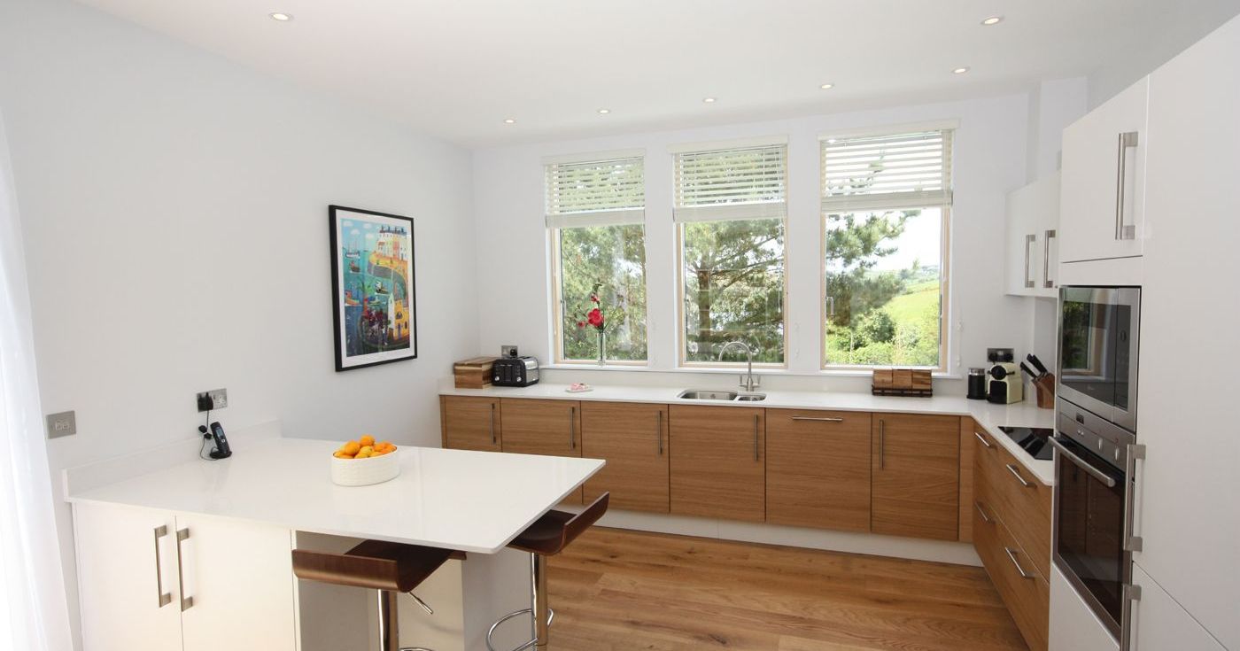 Modern kitchen with large windows, white countertops, and wooden cabinets.