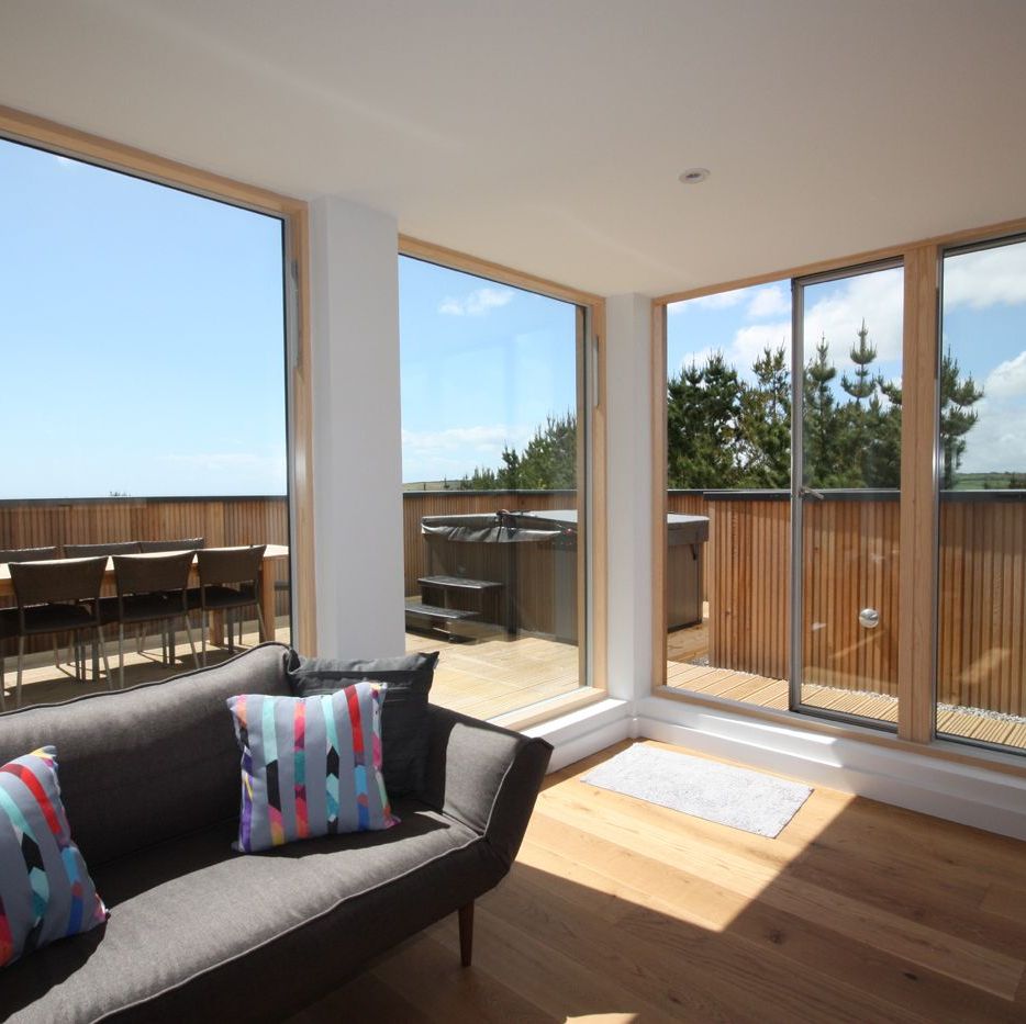 Bright modern living room with large glass windows and wooden deck outside.