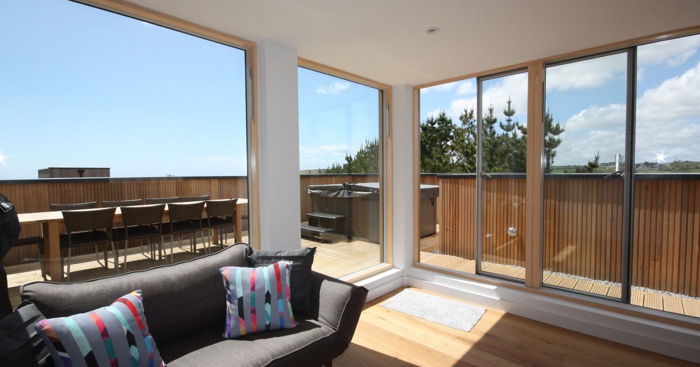Bright modern living room with large glass windows and wooden deck outside.