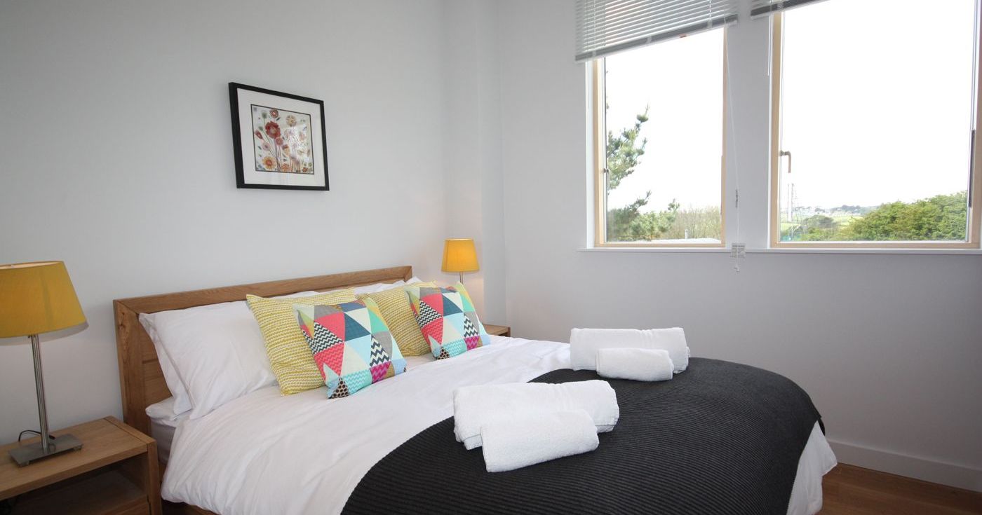 Modern bedroom with large window, bed, colorful pillows, and wall art