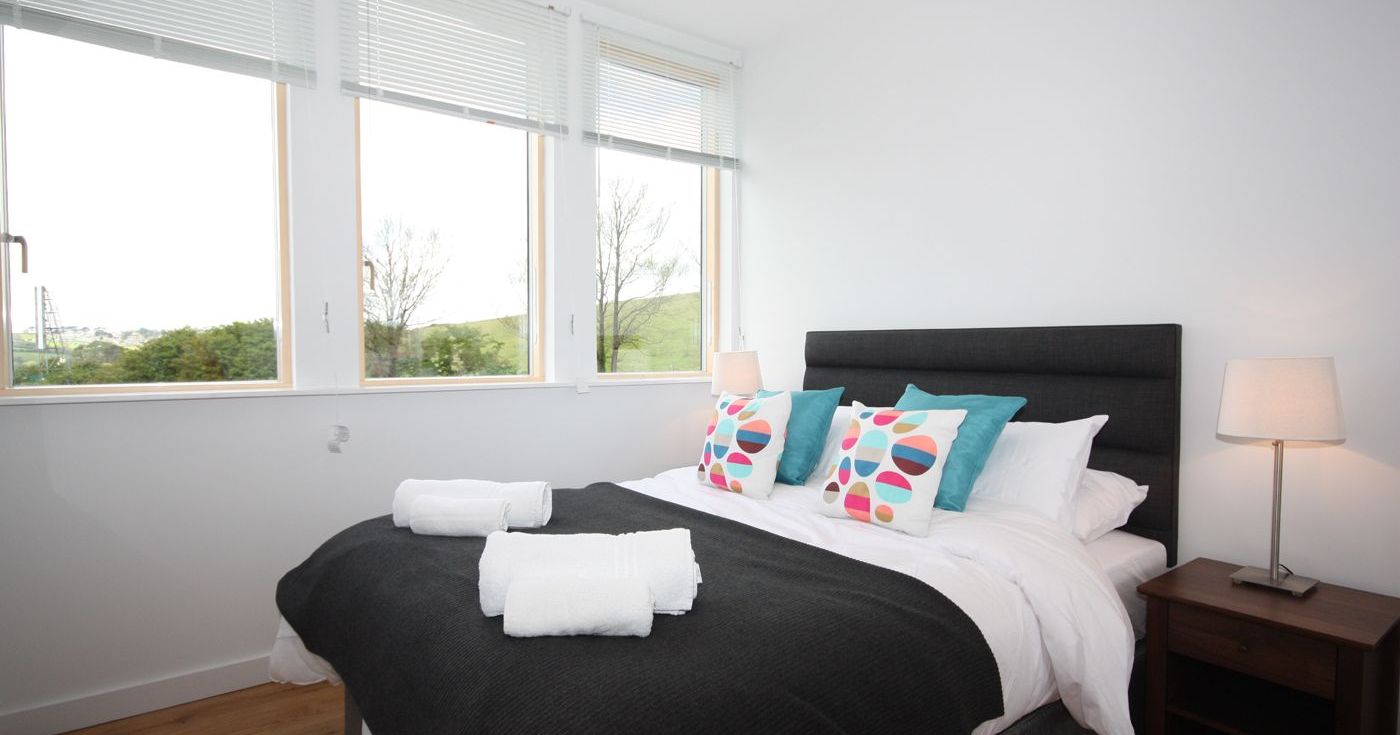 Modern bedroom with large windows, a neatly made bed, and colorful pillows