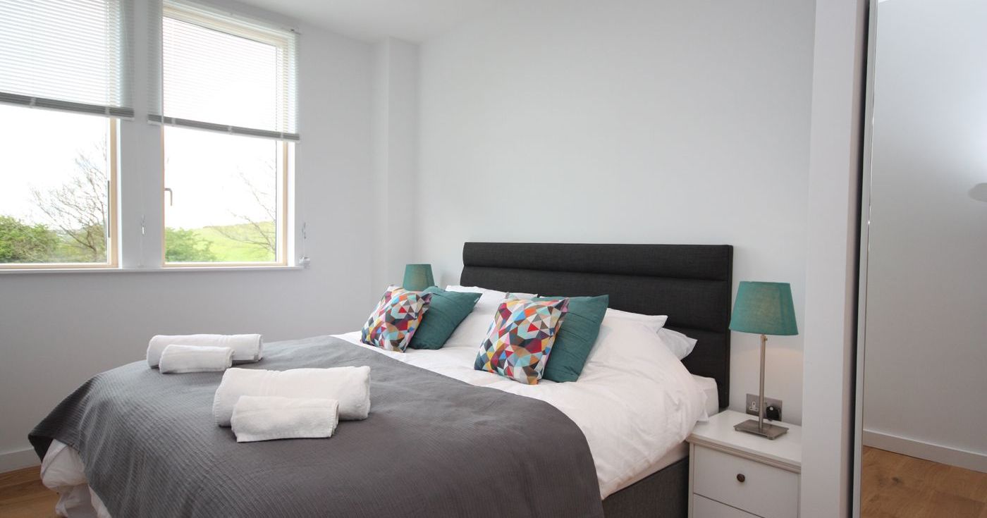 Modern bedroom with large bed, colorful pillows, bedside lamps, and large window