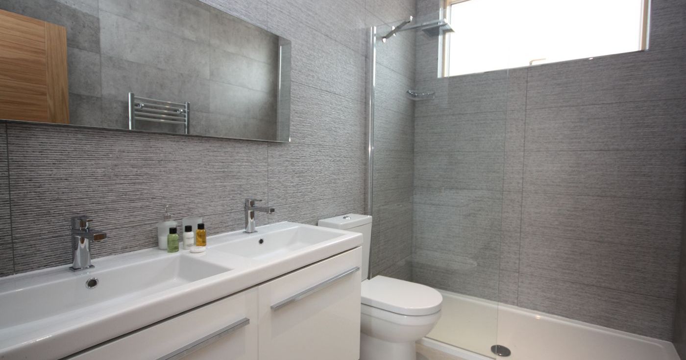 Modern bathroom with double sinks, toilet, and walk-in shower