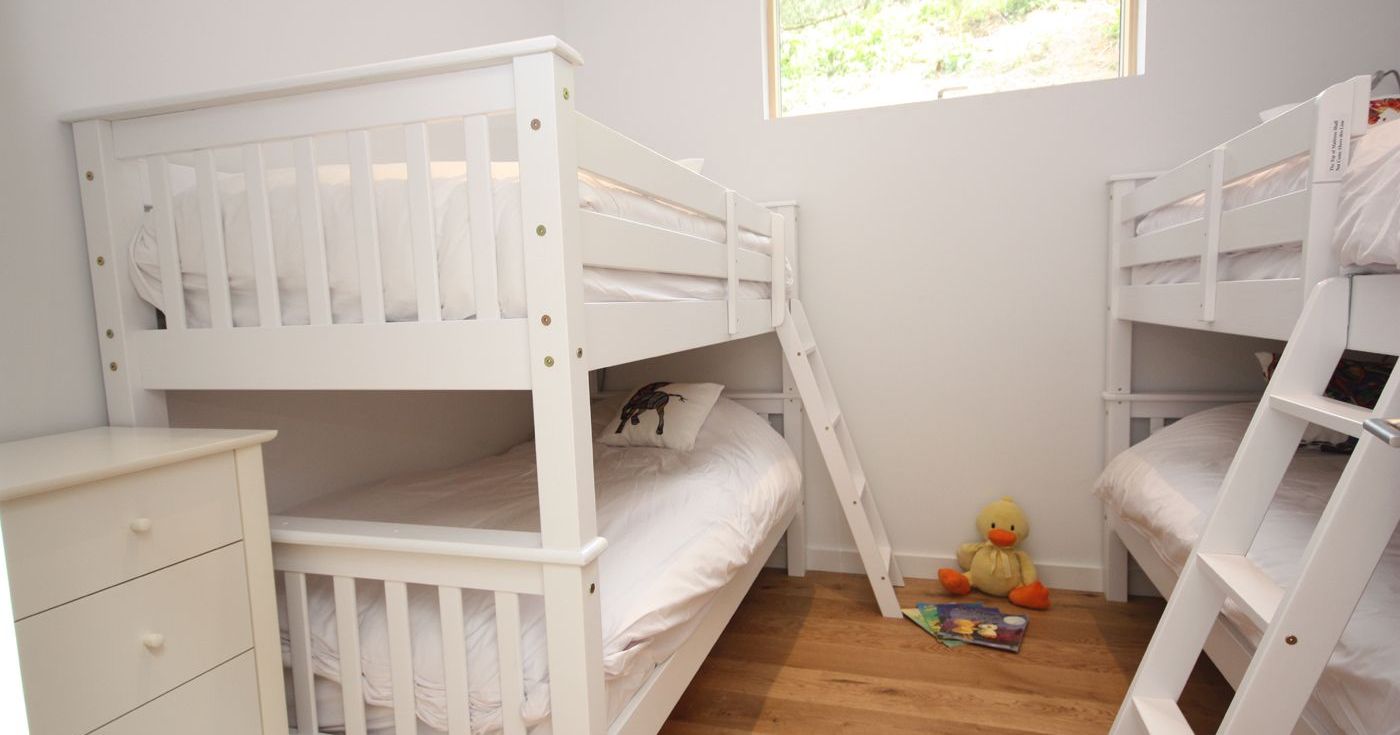 Children's bedroom with two white bunk beds, a window, a dresser, and toys on the floor