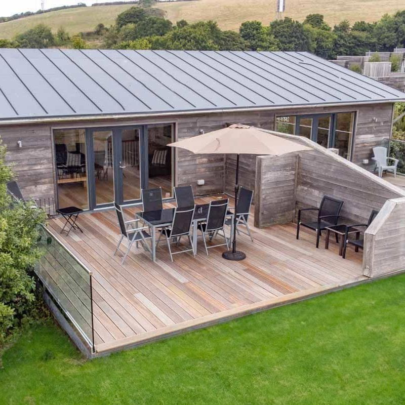 Modern wooden cabin with spacious outdoor deck area, dining furniture and umbrella