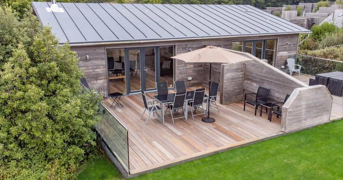 Modern wooden cabin with spacious outdoor deck area, dining furniture and umbrella