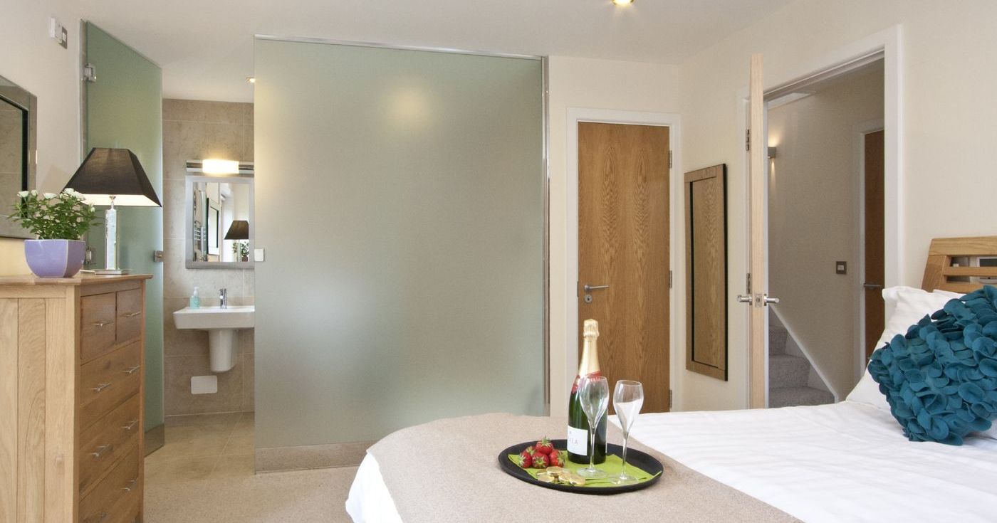 Modern bedroom with ensuite bathroom, champagne, and strawberries on bed