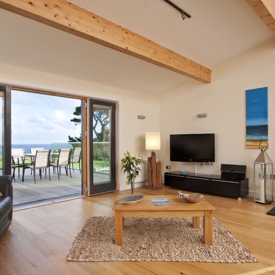 Modern living room with large glass doors opening to an outdoor dining area and ocean view