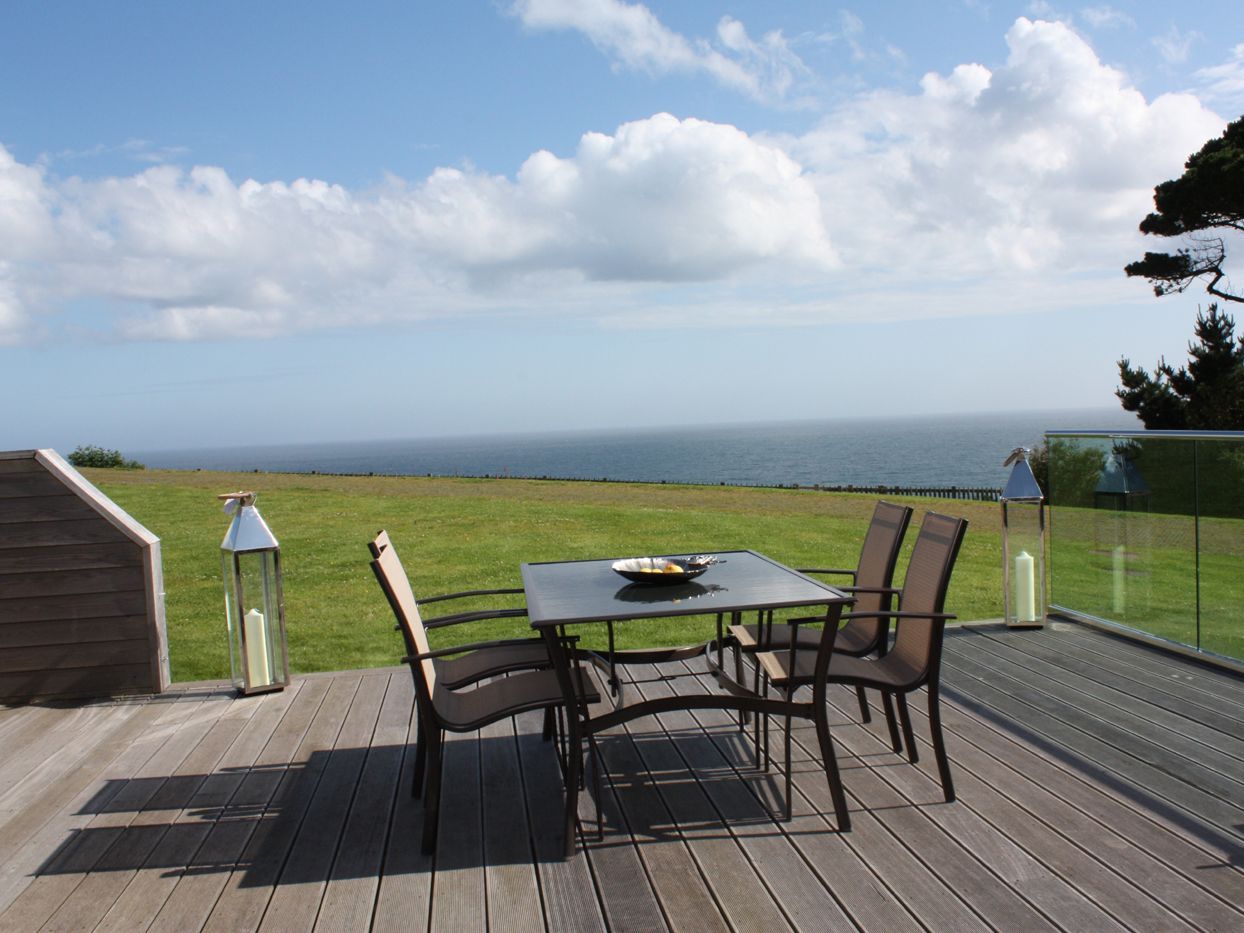 Outdoor dining set on a deck overlooking the ocean and grassy lawn
