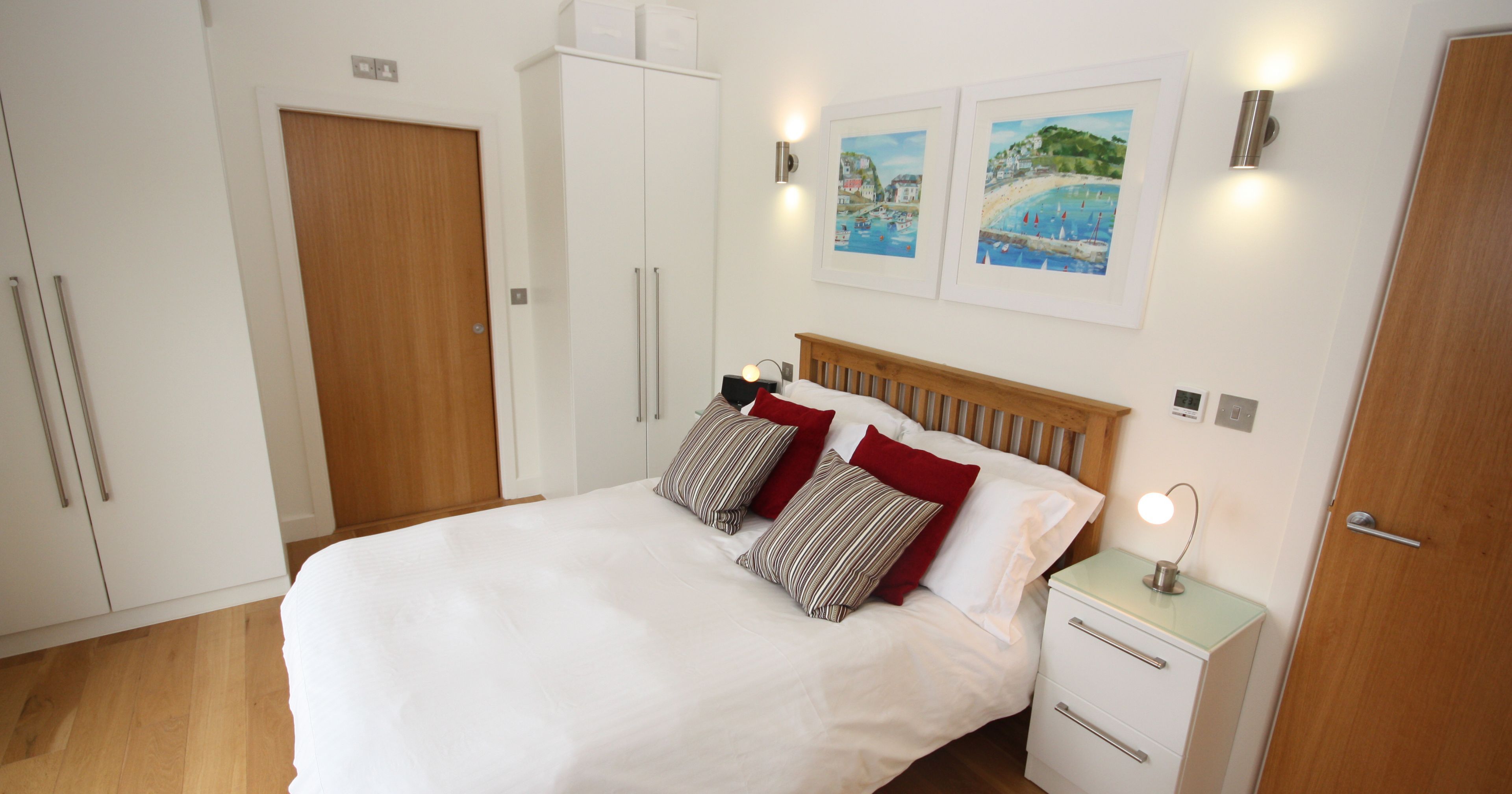 Modern bedroom with double bed, white linens, wooden headboard, bedside table, wardrobes, and wall art