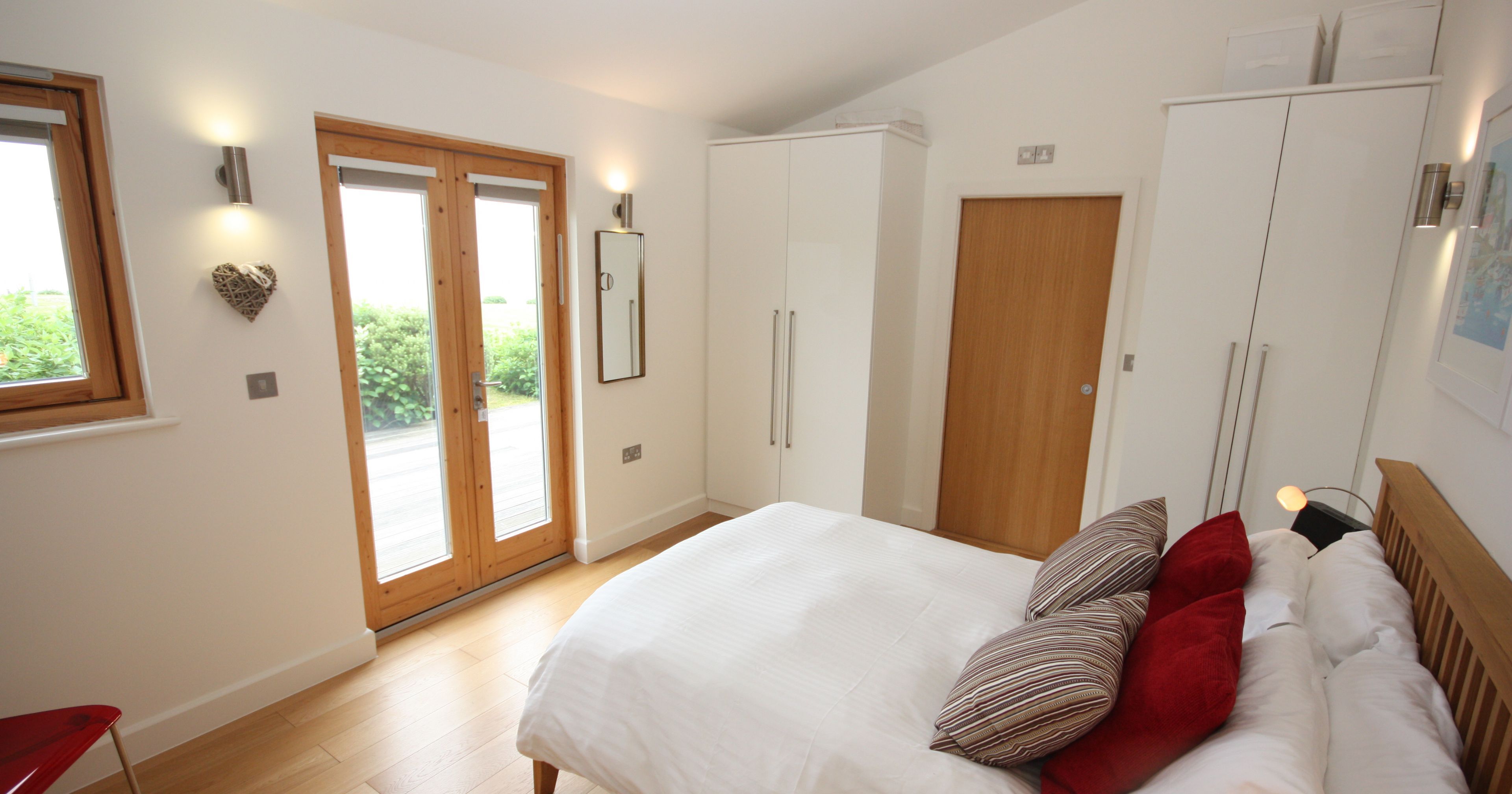 Modern bedroom with wooden floor, white bedding, and large wardrobes
