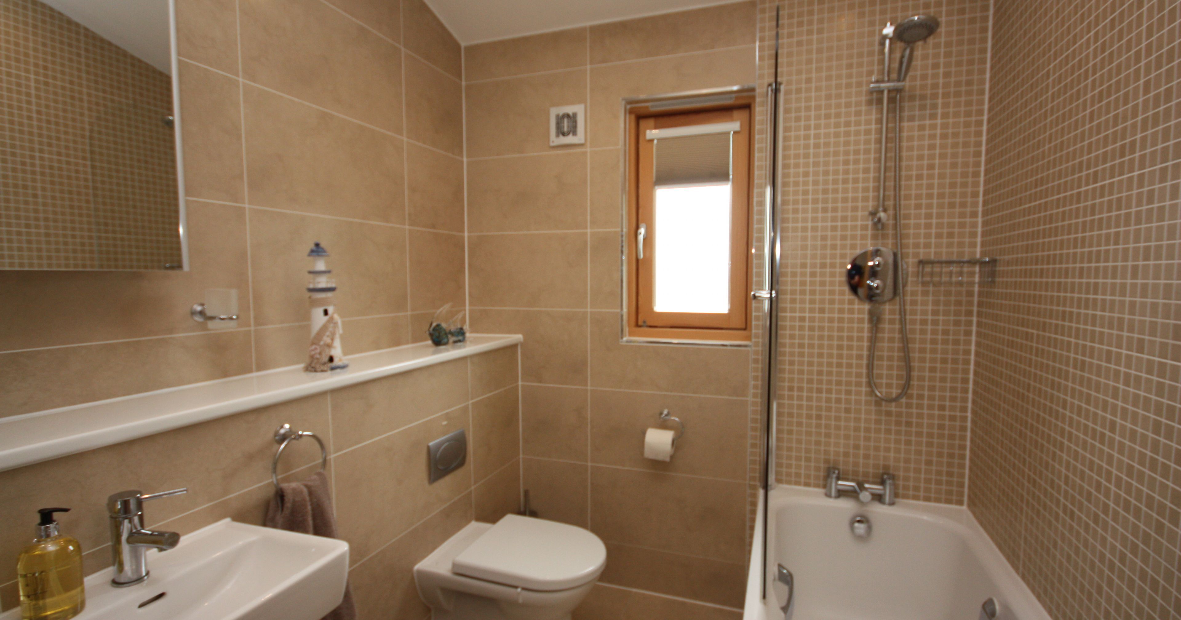 Modern bathroom with beige tiles, white bathtub, toilet, and sink