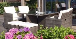 Outdoor patio set with white cushions and glass table, surrounded by blooming pink and purple hydrangeas.