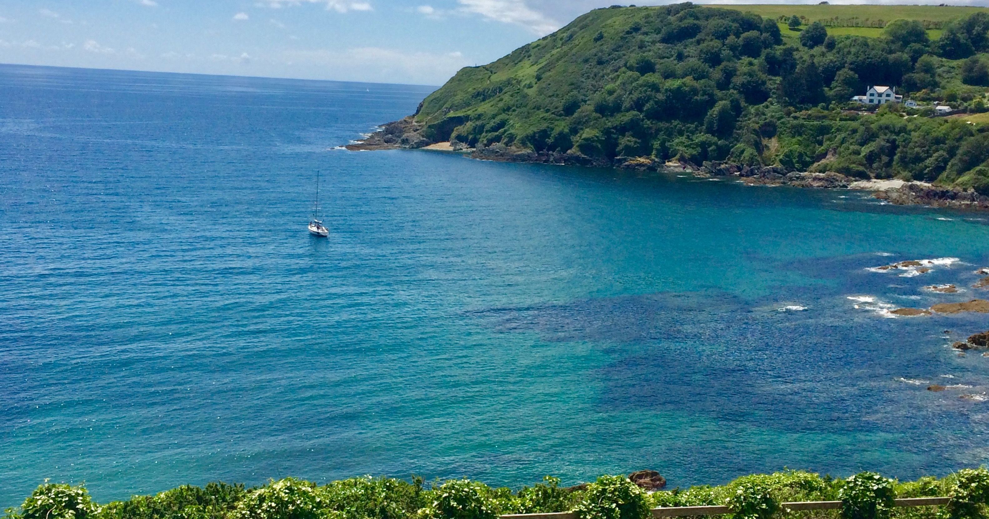 Scenic coastal view with a sailboat in blue waters and a green, hilly shoreline