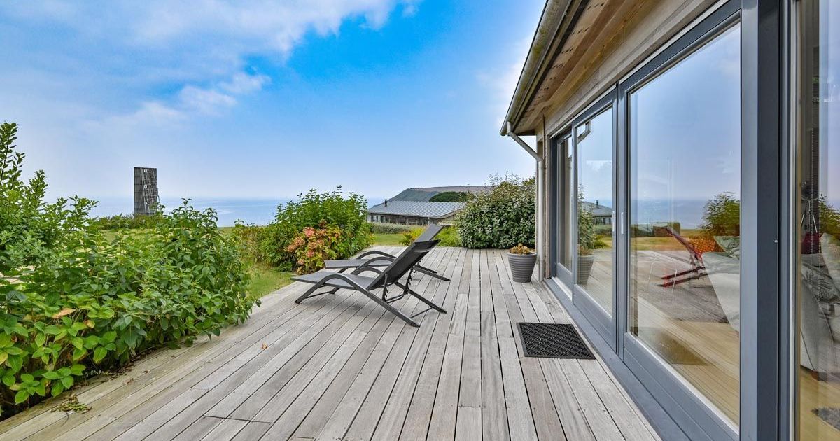 Modern wooden deck with lounge chairs overlooking the ocean and lush greenery.