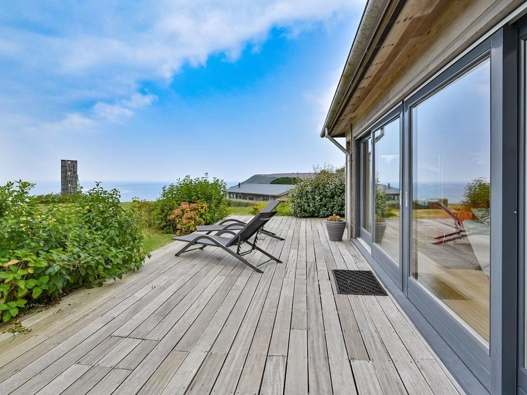 Modern wooden deck with lounge chairs overlooking the ocean and lush greenery.