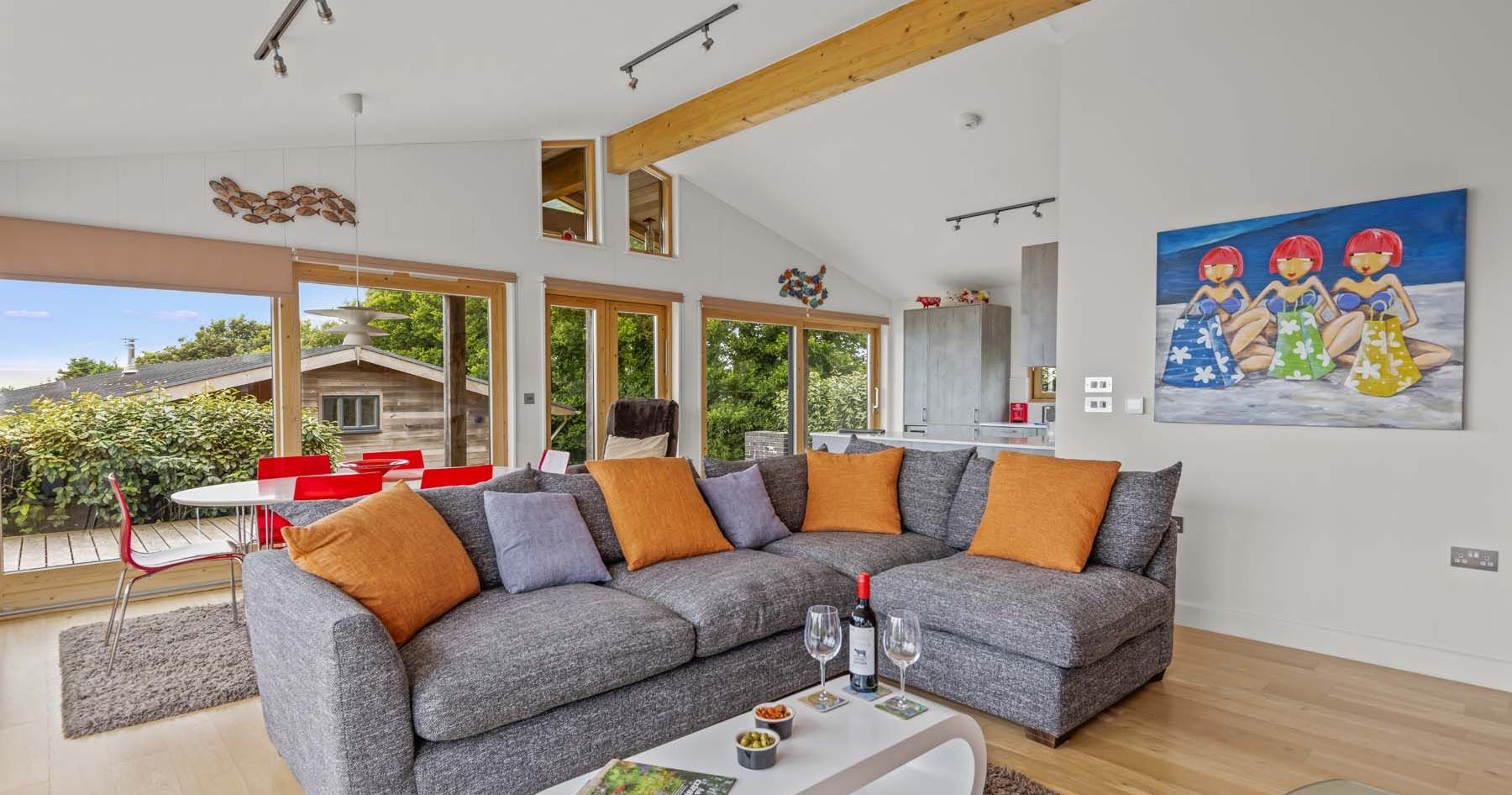 Modern living room with large grey sectional sofa, colorful pillows, wine on coffee table, and wall art of three women.