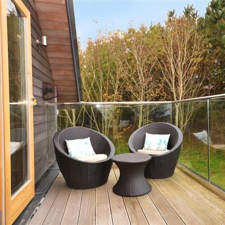 Modern balcony with two round wicker chairs and a small table, overlooking trees