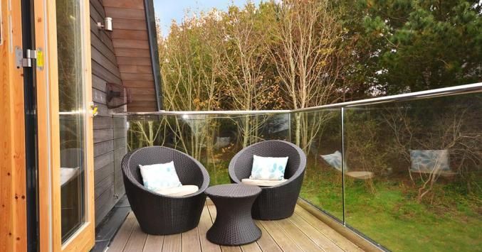 Modern balcony with two round wicker chairs and a small table, overlooking trees