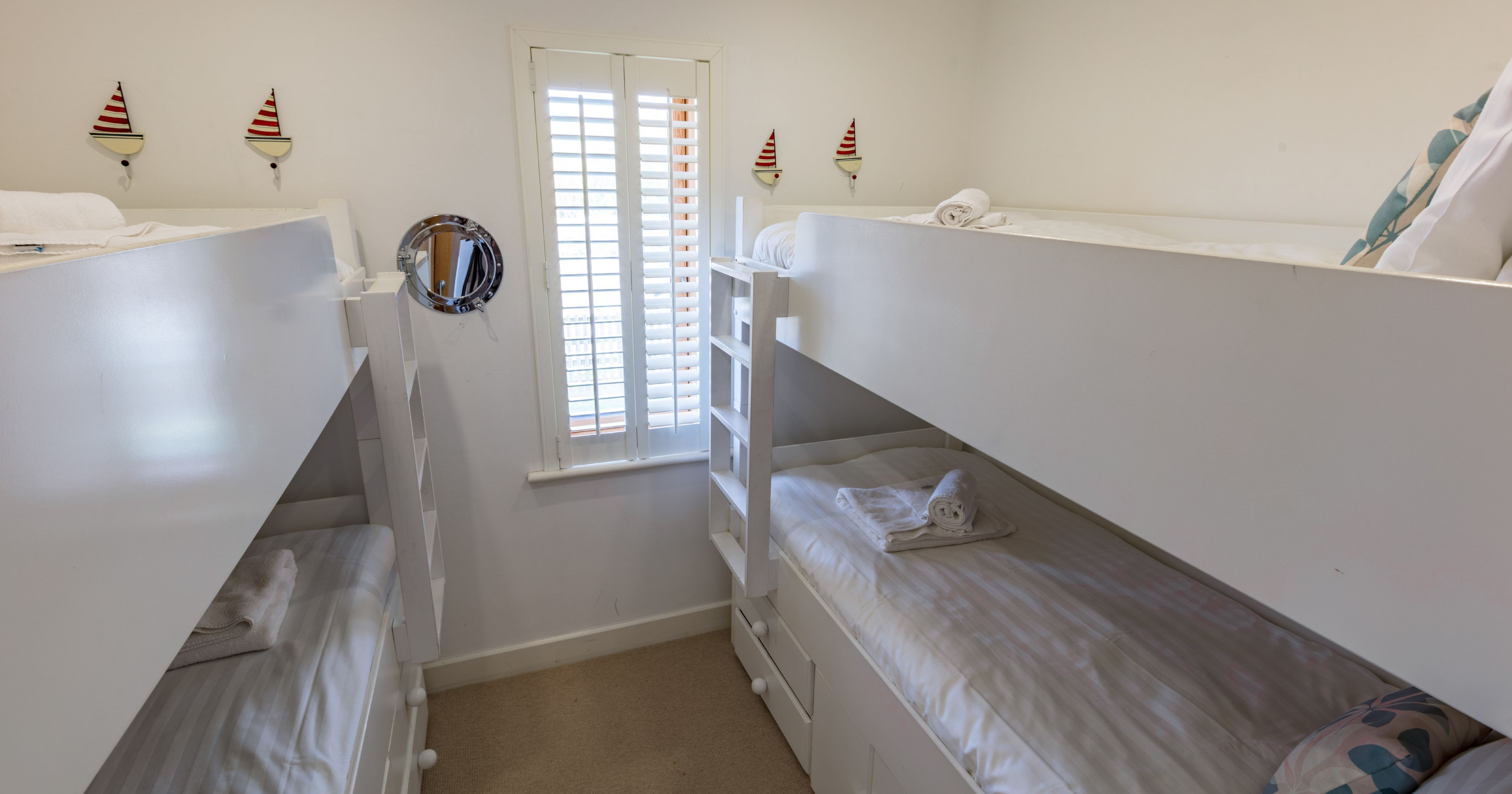 Small bedroom with two sets of white bunk beds and nautical decor