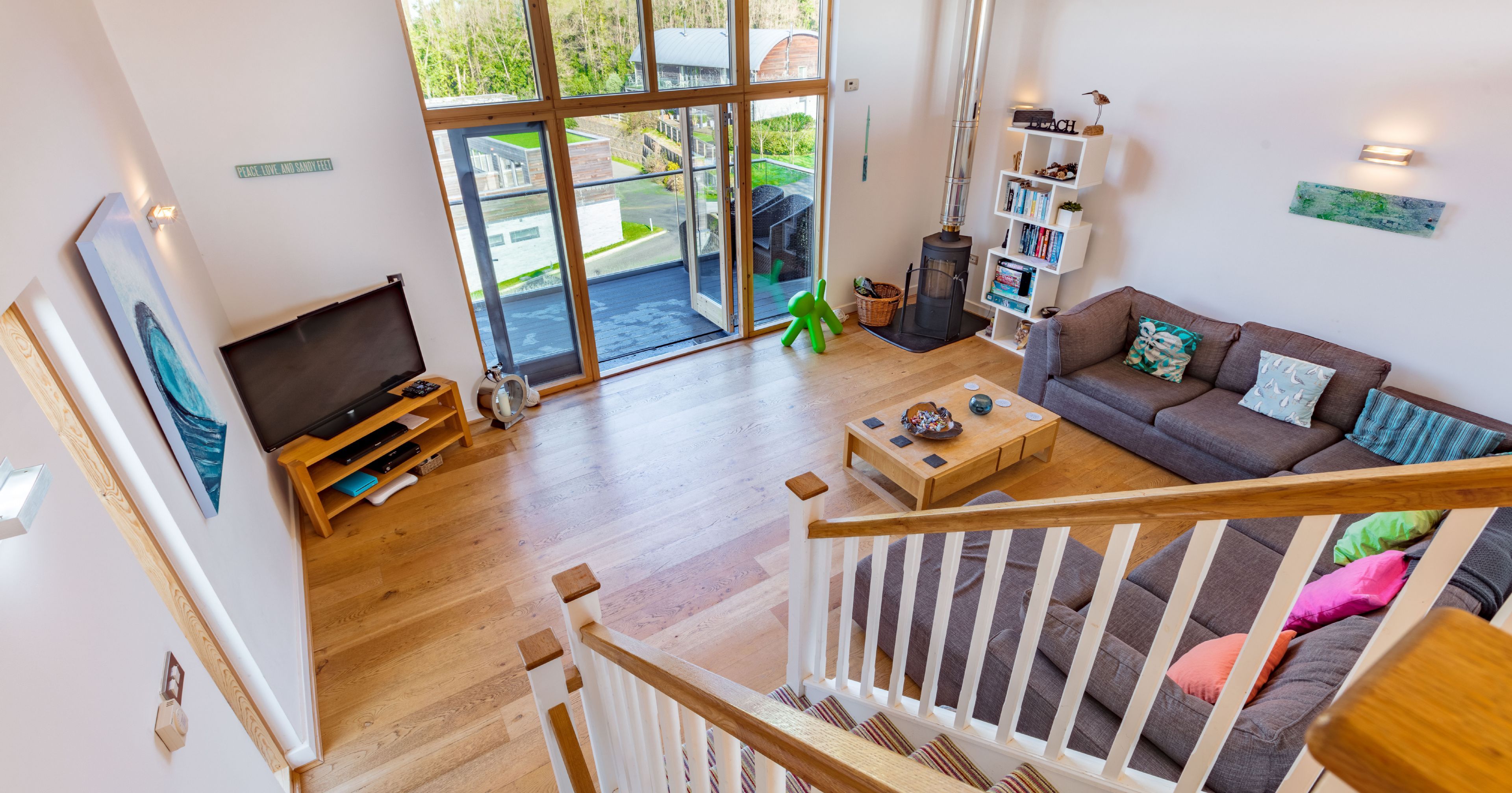 Modern living room with large windows, corner sofa, and wooden floors viewed from staircase