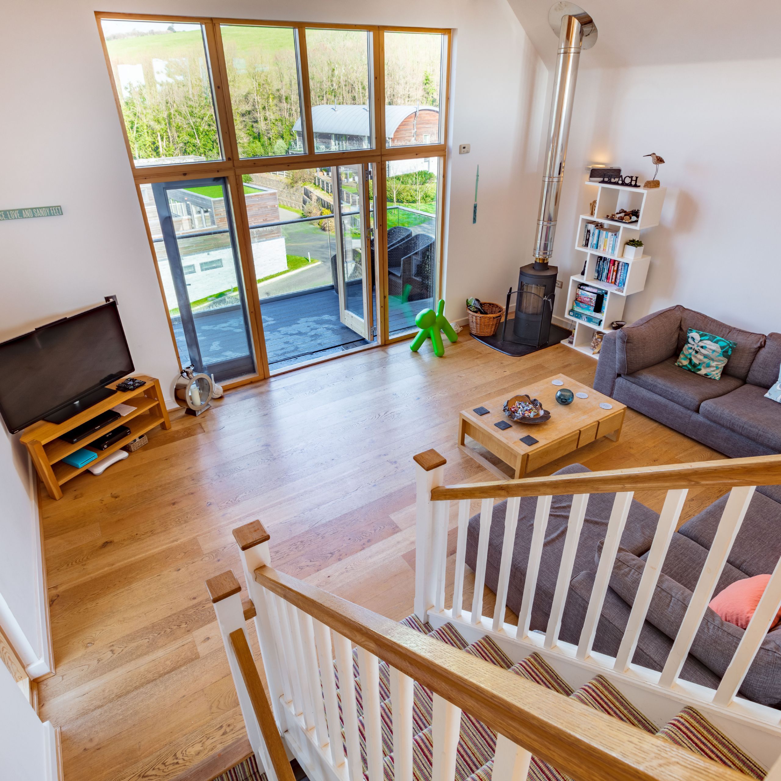 Modern living room with large windows, corner sofa, and wooden floors viewed from staircase