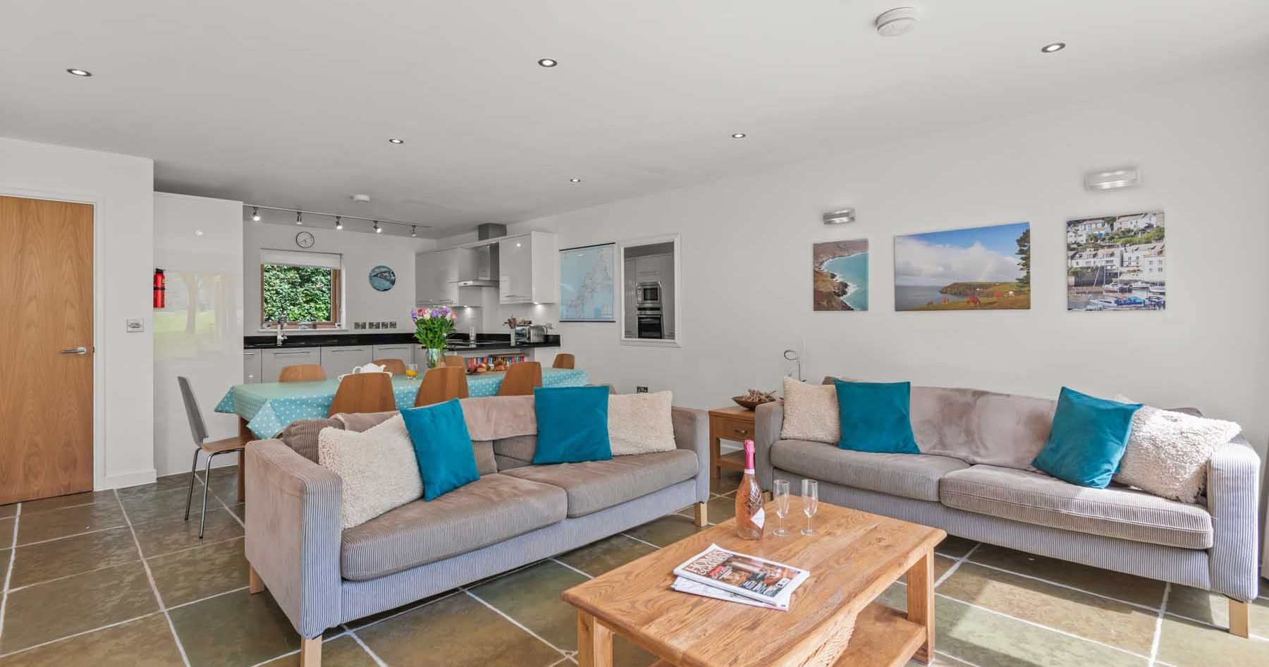 Modern open-plan living room and kitchen with two sofas, a wooden coffee table, and a dining area.