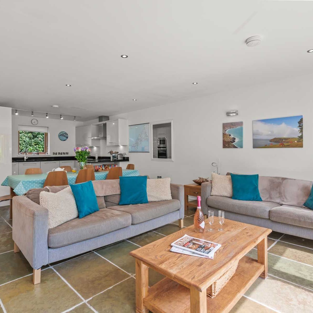 Modern open-plan living room and kitchen with two sofas, a wooden coffee table, and a dining area.