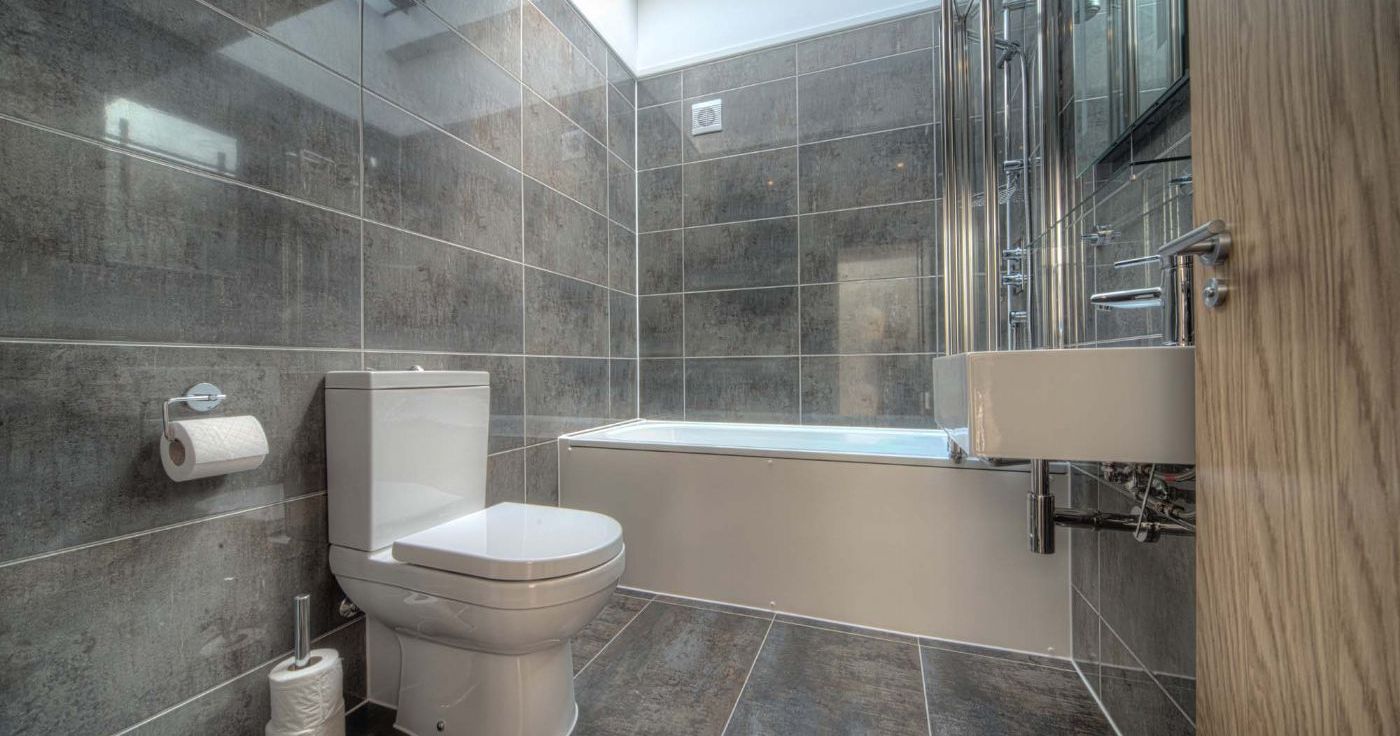 Modern bathroom with gray tile, toilet, bathtub, and skylight
