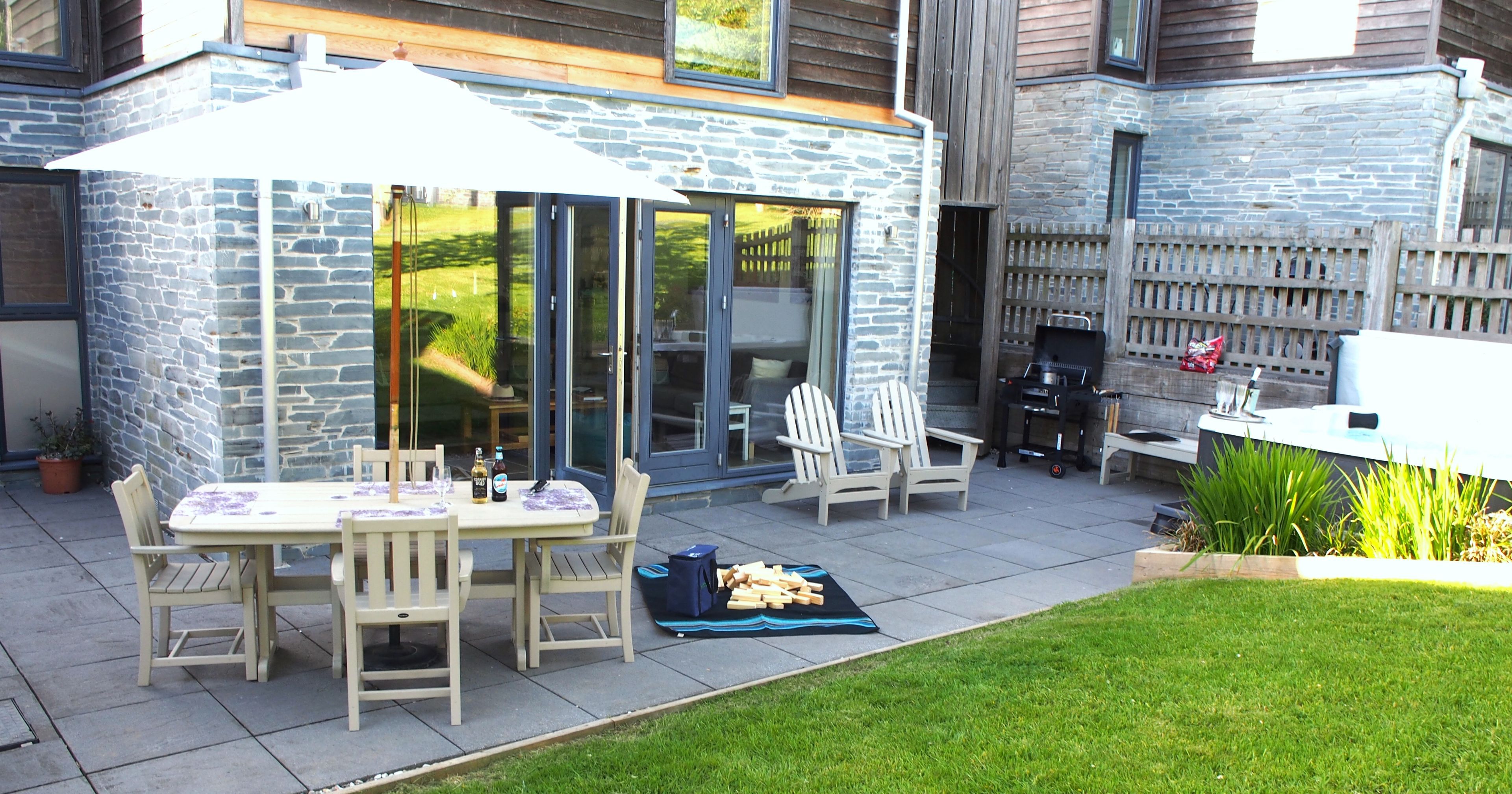 Modern stone patio with outdoor dining set, chairs, umbrella, barbecue grill, and grassy yard