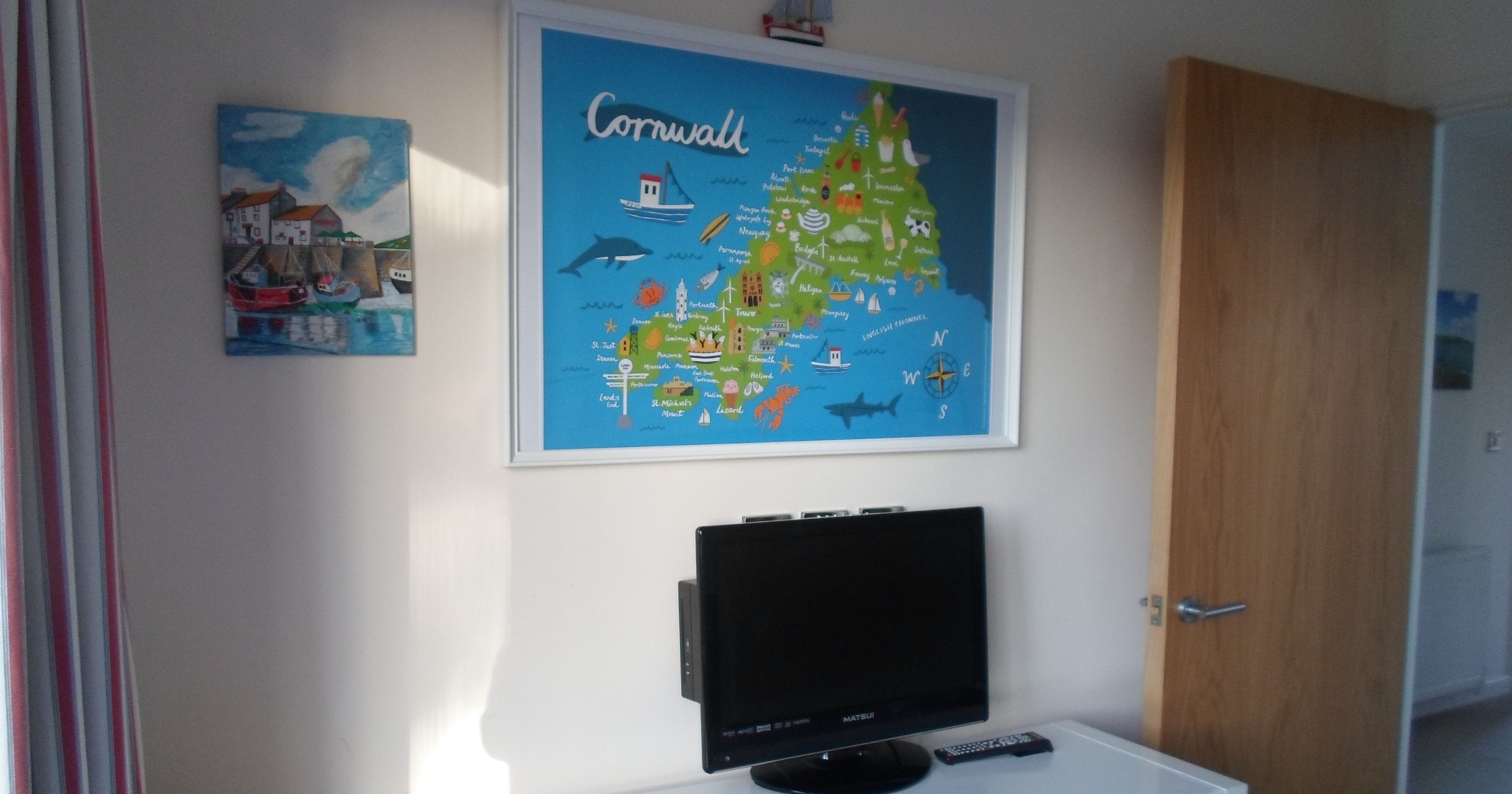 Room with a TV, a Cornwall map on the wall, and a white cabinet