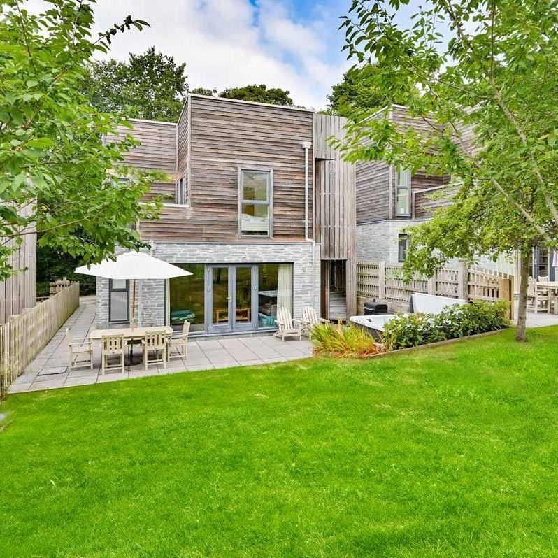 Modern townhouse with wooden and brick exterior, patio, outdoor furniture, and green lawn.