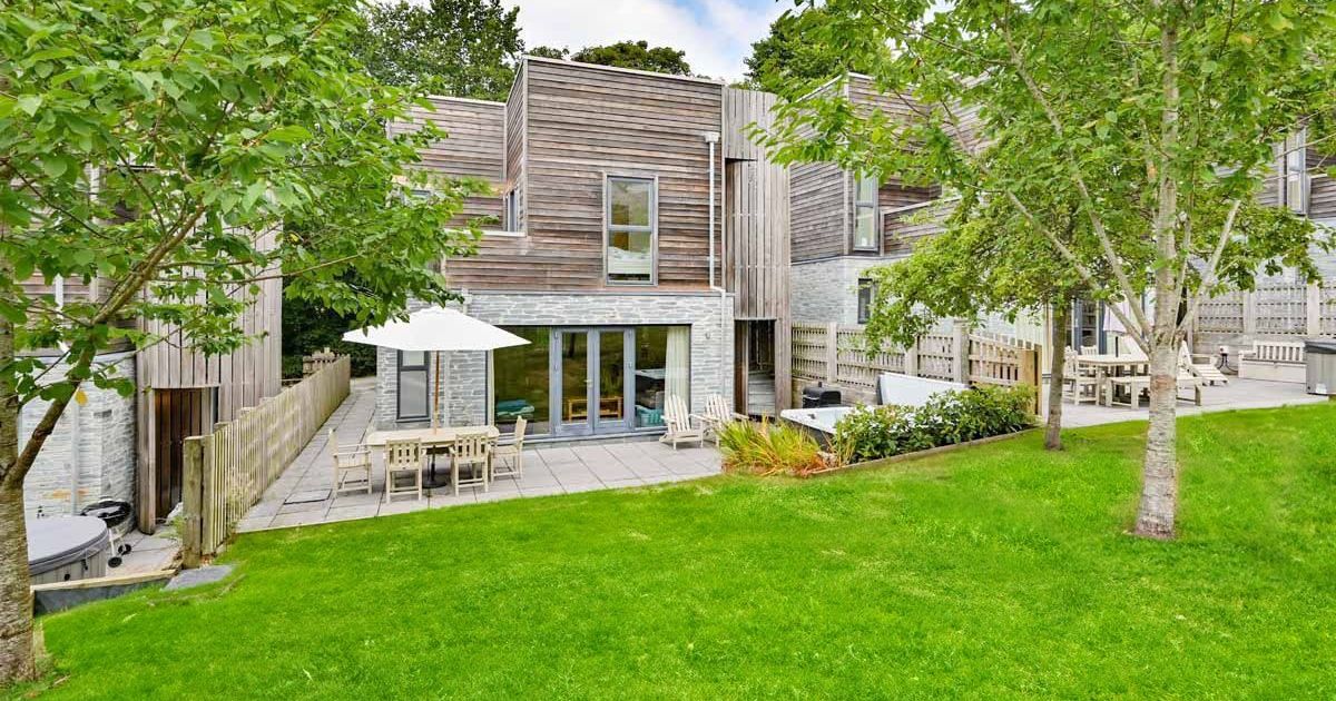 Modern townhouse with wooden and brick exterior, patio, outdoor furniture, and green lawn.