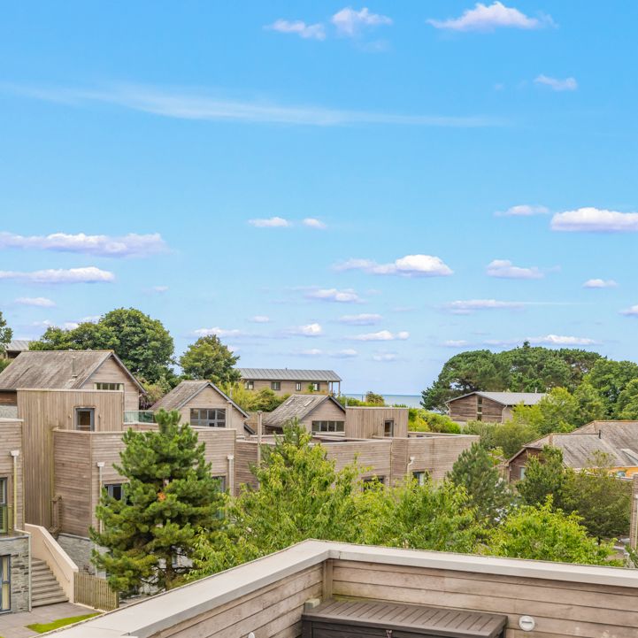 A scenic view of modern wooden houses surrounded by greenery and trees under a bright blue sky with scattered clouds.