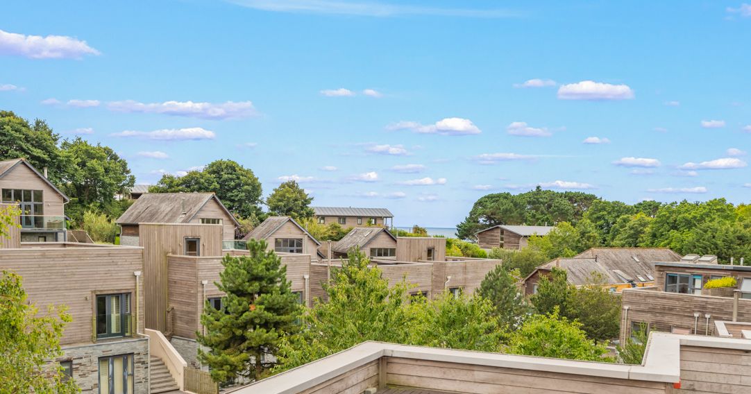 A scenic view of modern wooden houses surrounded by greenery and trees under a bright blue sky with scattered clouds.