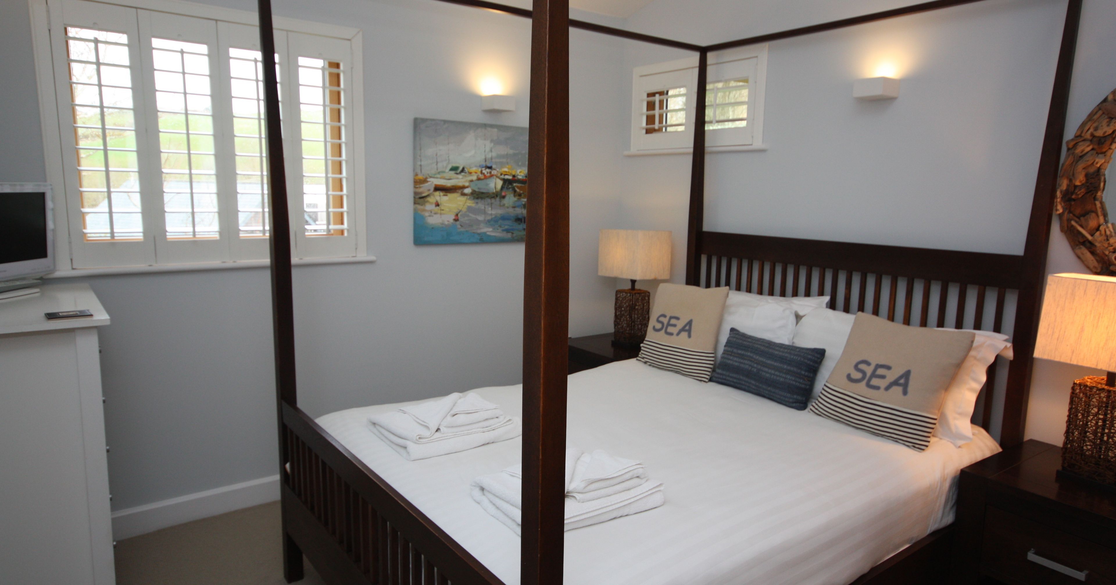 Cozy bedroom with four-poster bed, white linens, and nautical-themed pillows.