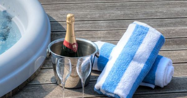 Champagne bottle in ice bucket with two glasses and blue striped towels beside a hot tub