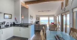 Open-plan kitchen, dining, and living space with large windows overlooking the sea.
