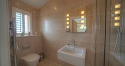 Modern bathroom with beige tiles, wall-mounted sink, toilet, and illuminated mirror