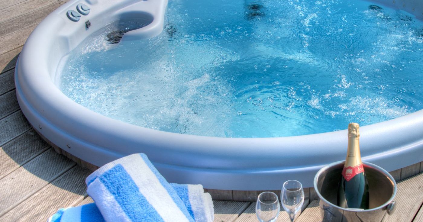 Outdoor hot tub with bubbling water next to rolled towels, champagne bottle in a bucket, and two glasses.